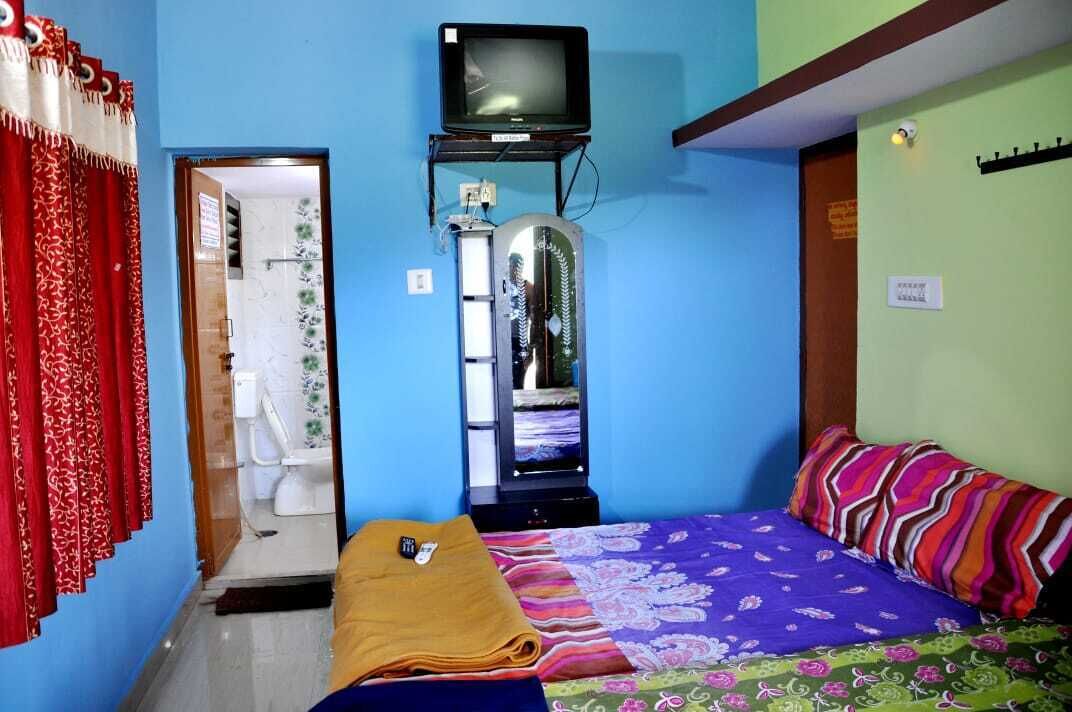 Ein Schlafzimmer mit Bett, Fernseher auf einem Schrank, einem Spiegel und einem durchgehenden Türrahmen sichtbaren Badezimmer.