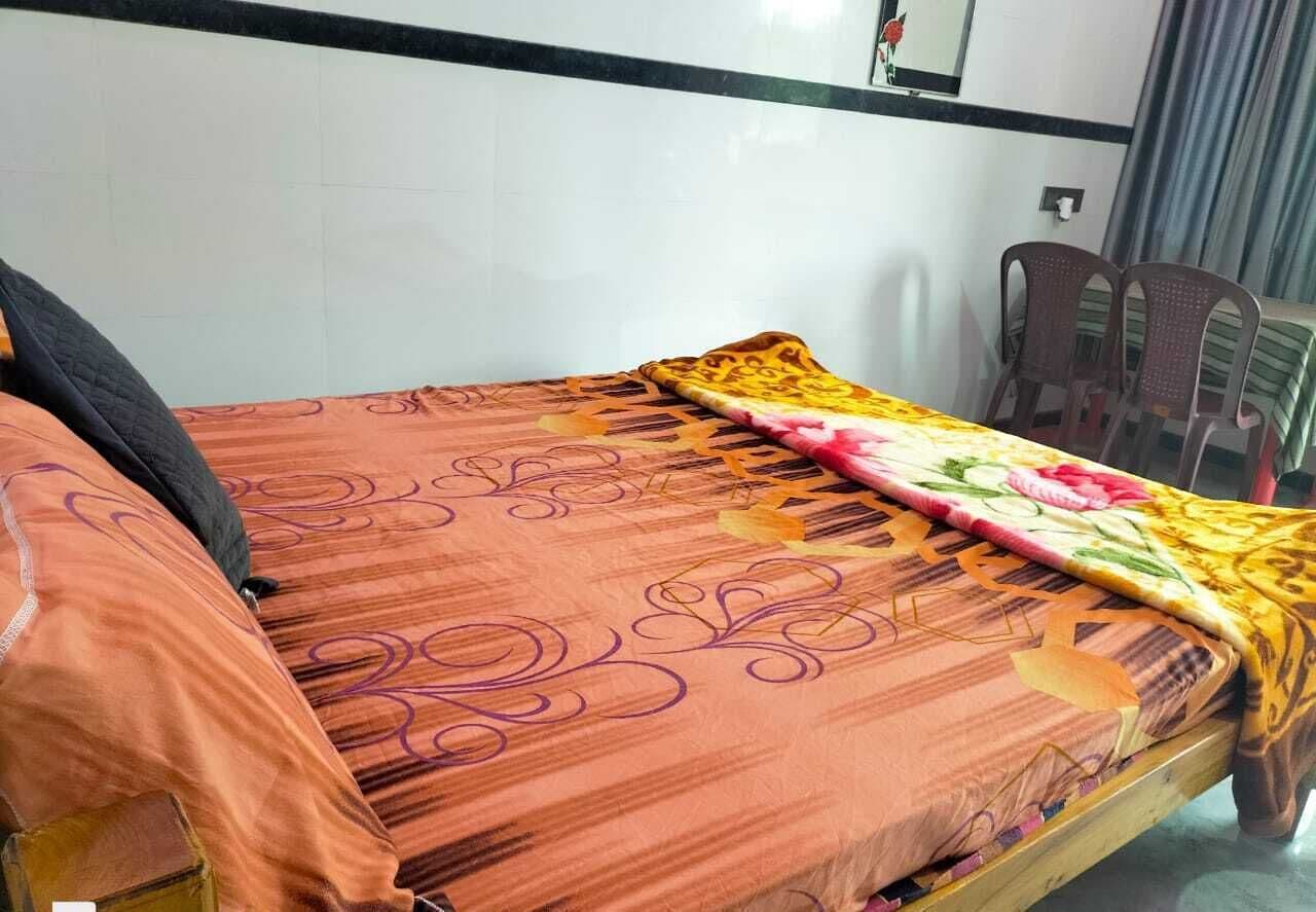 A single bed with a patterned bedspread, a pillow, and a blanket. There are two chairs and a small table in the room.