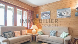 A cozy room with two sofas, a table, and a lamp. There are wooden walls and pictures of mountains. - Charmant appartement de 3 pièces au 1er étage de l'immeuble "Les Roches" à proximité du centre du vi (Chandolin)