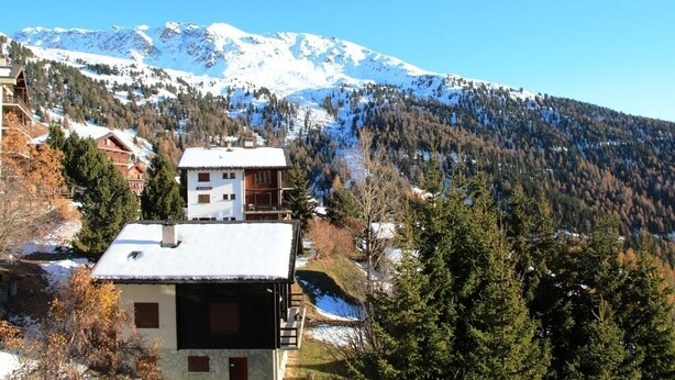 A mountain cabin with a balcony, surrounded by snow-covered trees and mountains.