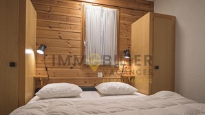 A bedroom with a wooden headboard, two bedside lamps, a window with curtains, and a bed with white bedding.