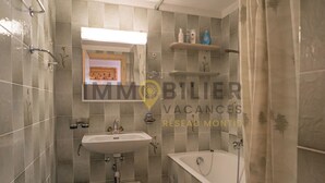 A bathroom with a sink, toilet, and bathtub. There are shelves with toiletries and a shower curtain.