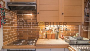 A kitchen with a brick backsplash, wooden cabinets, a stove, and various kitchen utensils.