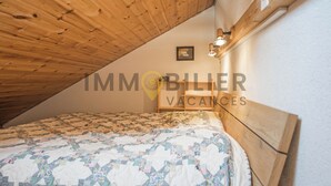A bedroom with a wooden ceiling, a bed with a floral quilt, and a nightstand with a lamp.