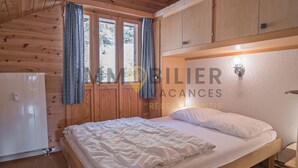 Ein schlichtes Schlafzimmer im Chalet-Stil mit Bett, Vorhängen und einer Wandleuchte.