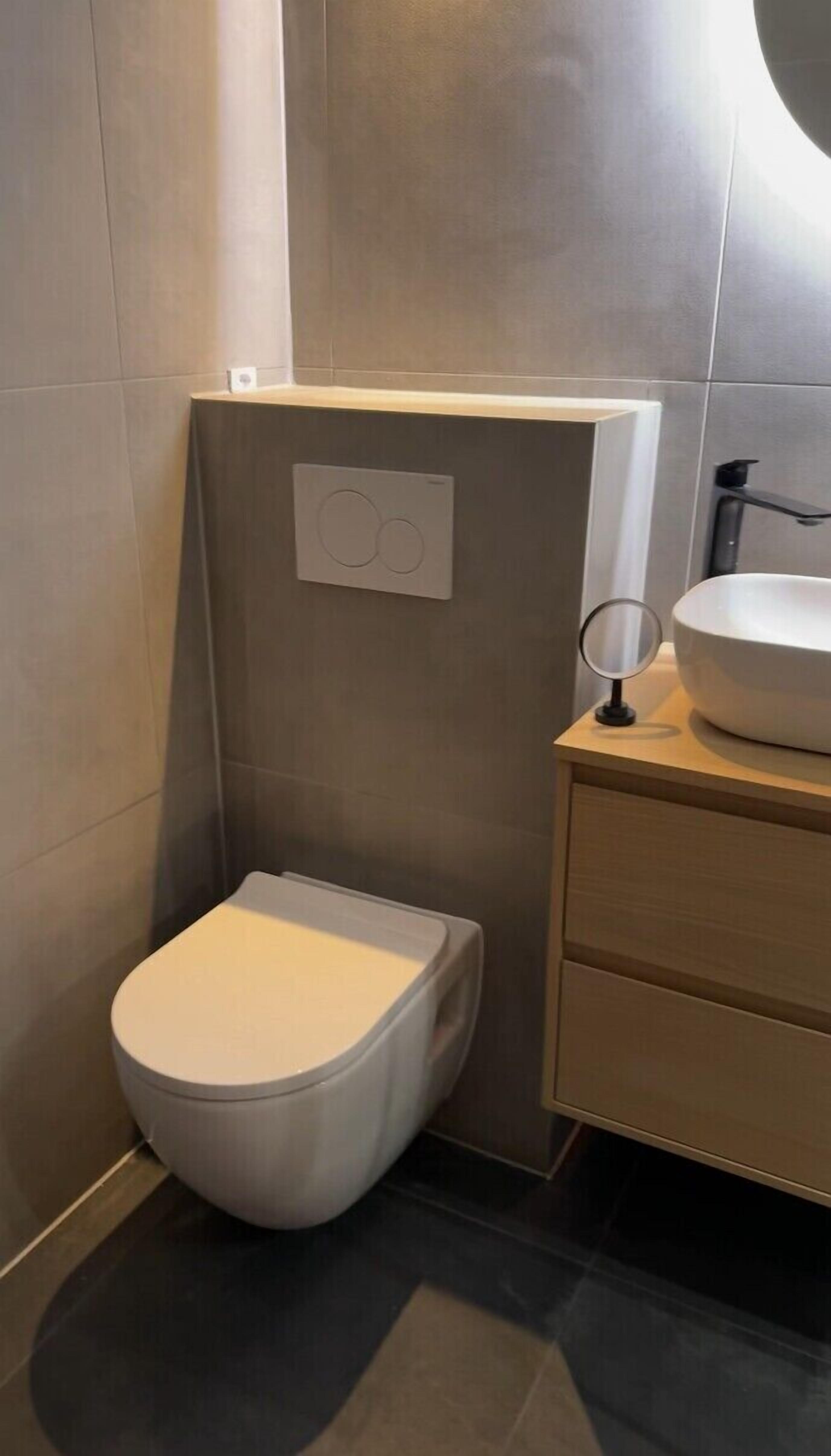 Een moderne badkamer met toilet, een spiegel aan de muur en een wastafel.
