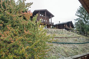 Una baita di legno con un balcone, immersa tra alberi e un pendio erboso.