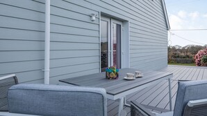 A deck with a table and chairs, a window, and a view of the surrounding area. - Bryn Derw (Caernarfon)