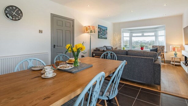 A modern dining area with a wooden table, blue chairs, and a clock on the wall. - Bryn Derw (Caernarfon)