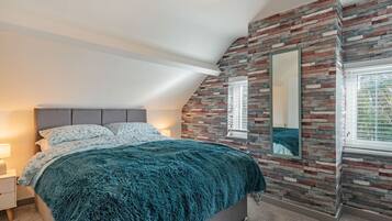 A bedroom with a bed, a nightstand, a wall-mounted mirror, and a window with blinds.