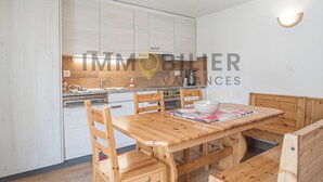 A modern kitchen with white cabinets, a wooden dining table, and a bowl on the table. - Très agréable 2 pièces contemporain, idéal pour 2 à 4 personnes, situé dans une petite résidence de (St-Luc)