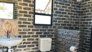 Un baño con pared de ladrillo, ventana, lavamanos, inodoro y ducha.