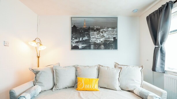 A neatly made bed with a pillow that reads "Smile" and a cityscape painting above it.
