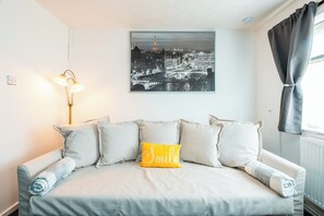 A neatly made bed with a pillow that reads "Smile" and a cityscape painting above it.