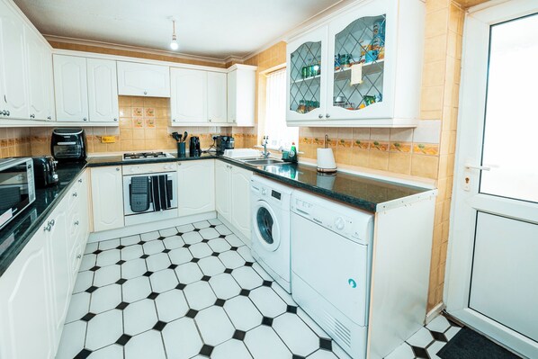 A kitchen with white cabinets, a black and white tiled floor, a washing machine, and a coffee maker.