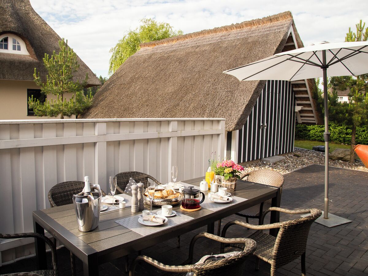 An outdoor dining area with a table set for breakfast, including a pitcher, cups, and a basket of pastries.