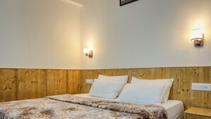 Un lit double avec une couvre-lit à motifs, une tête de lit en bois, deux appliques murales et une table de chevet avec un tiroir.