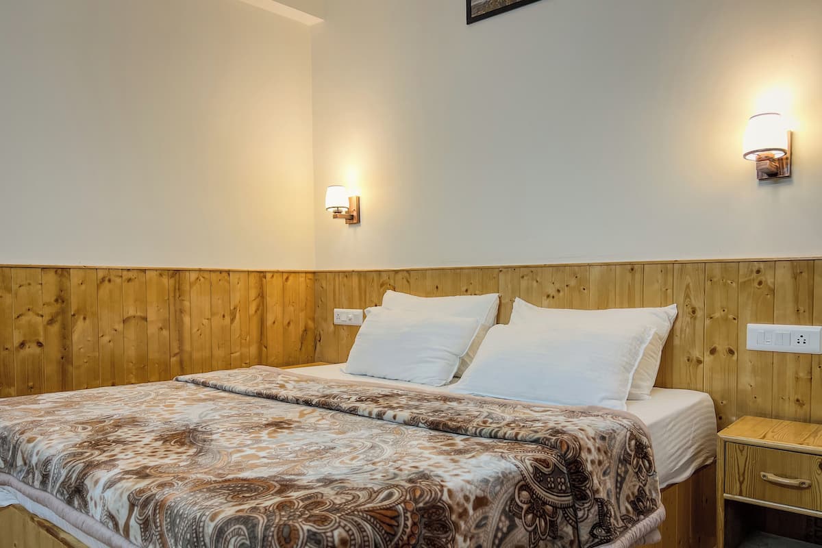 A double bed with a patterned bedspread, wooden headboard, two wall-mounted light fixtures, and a nightstand with a drawer.