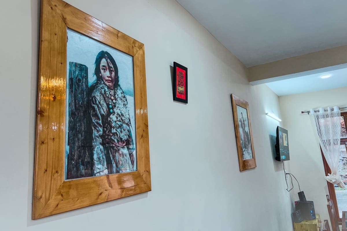 A room with wooden-framed artwork on the wall, a small motivational poster, and a wall-mounted device.