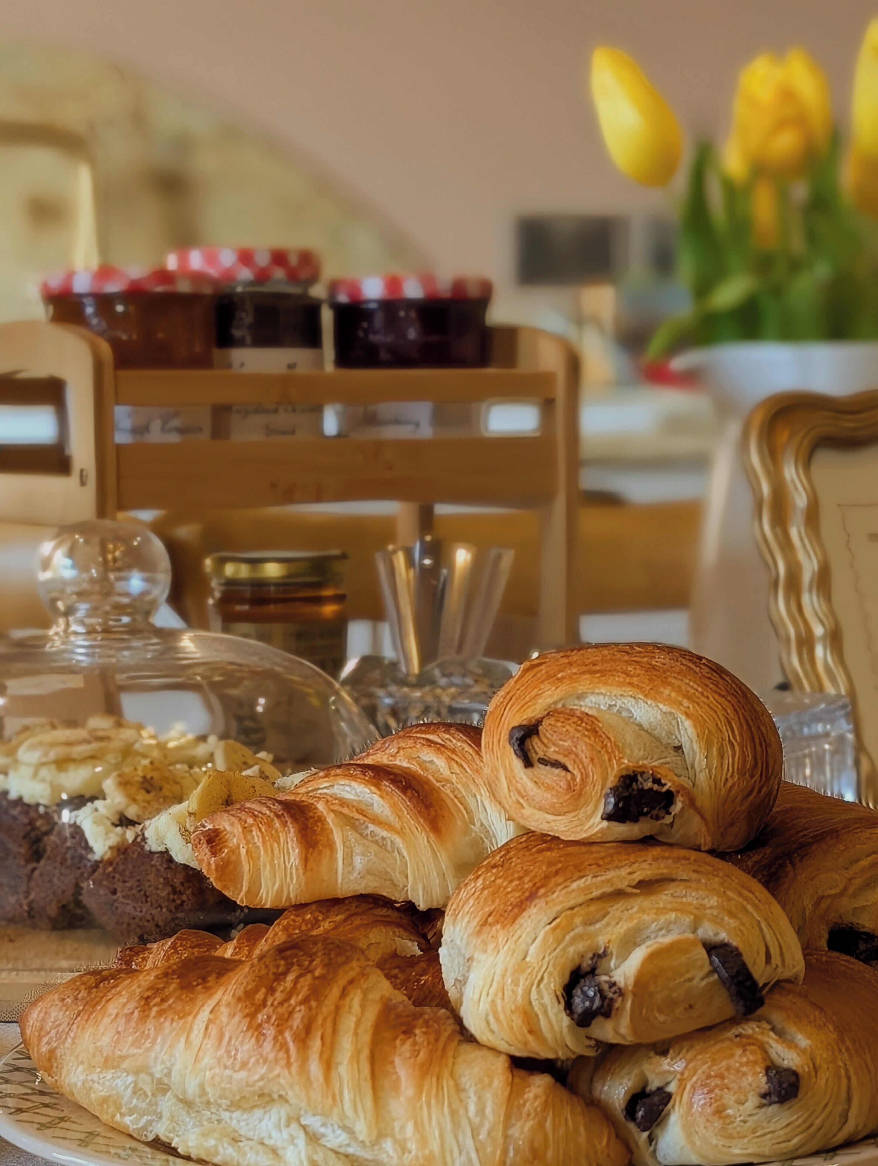 Uma mesa com doces, um recipiente de vidro e uma cadeira com toalha quadriculada vermelha e branca.