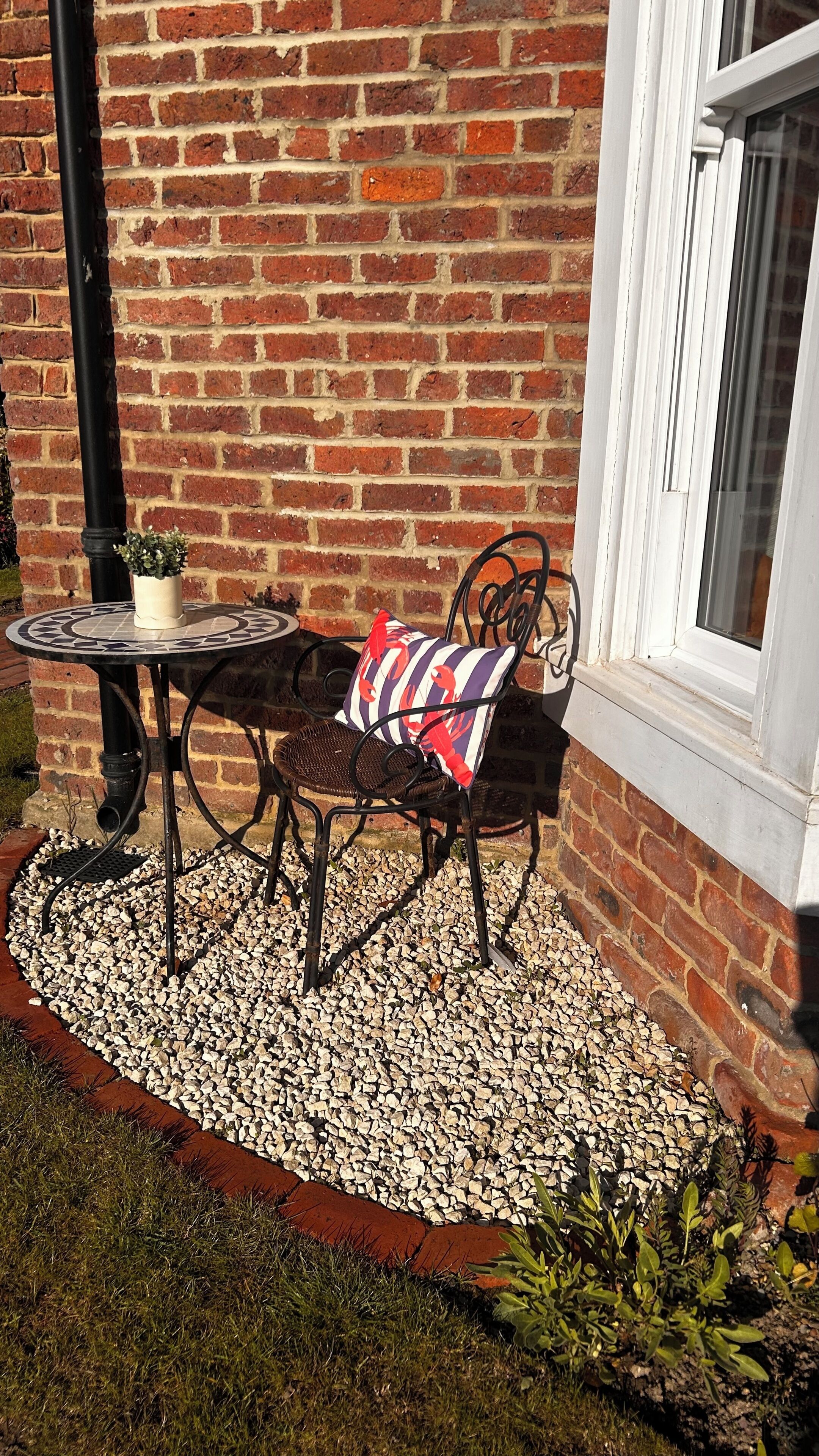 A patio with a table and chair, a brick wall, and a window.
