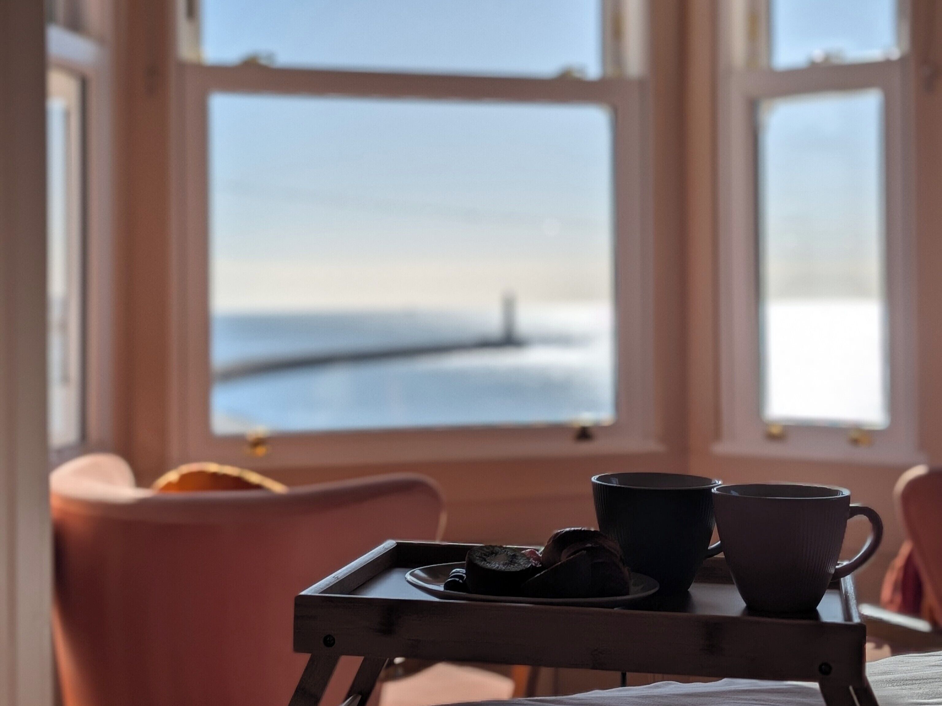 A room with a table set for two, a window with a view of the sea, and a chair.