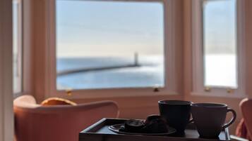 A room with a table set for two, a window with a view of the sea, and a chair.