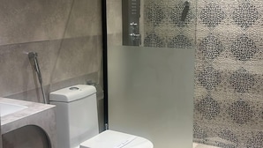 A modern bathroom with a toilet, shower, and a patterned wall. - Anaf Hotel (Madinah)