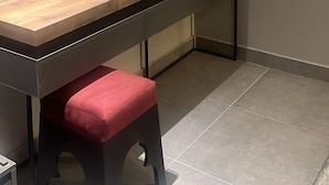A room with a wooden desk, a red cushioned stool, a wall-mounted mirror, and an air conditioning unit. - Anaf Hotel (Madinah)