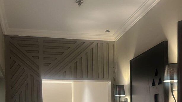 A hotel room with a bed, a wall-mounted TV, and a patterned carpet. - Anaf Hotel (Madinah)