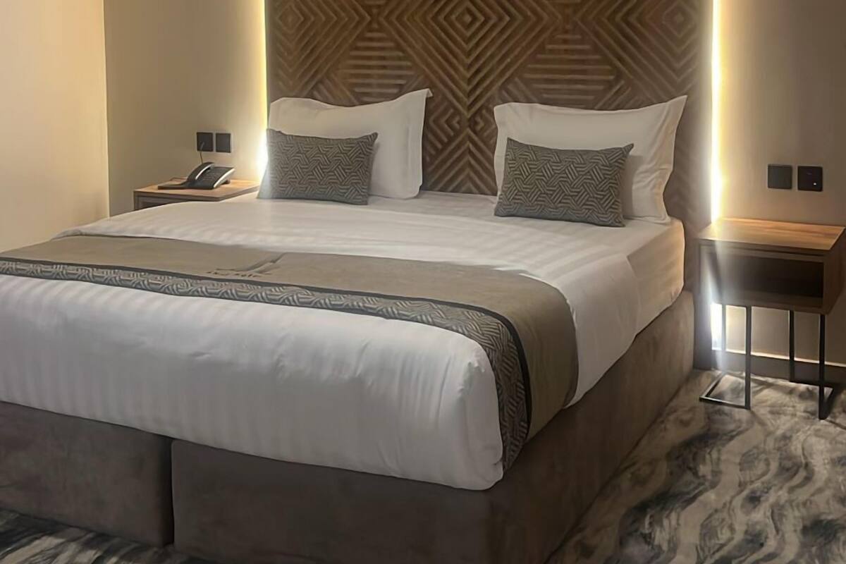 A modern hotel room with a large bed, a ceiling fan, an air conditioning unit, and a patterned wall.
