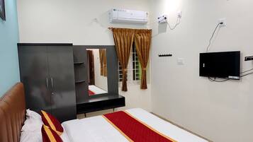 A hotel room with a bed, a wardrobe, a mirror, an air conditioning unit, a television, and a window with curtains.