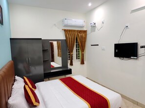 A hotel room with a bed, a wardrobe, a mirror, an air conditioning unit, a television, and a window with curtains. - ARUVI RESORT (Kolli Hills)