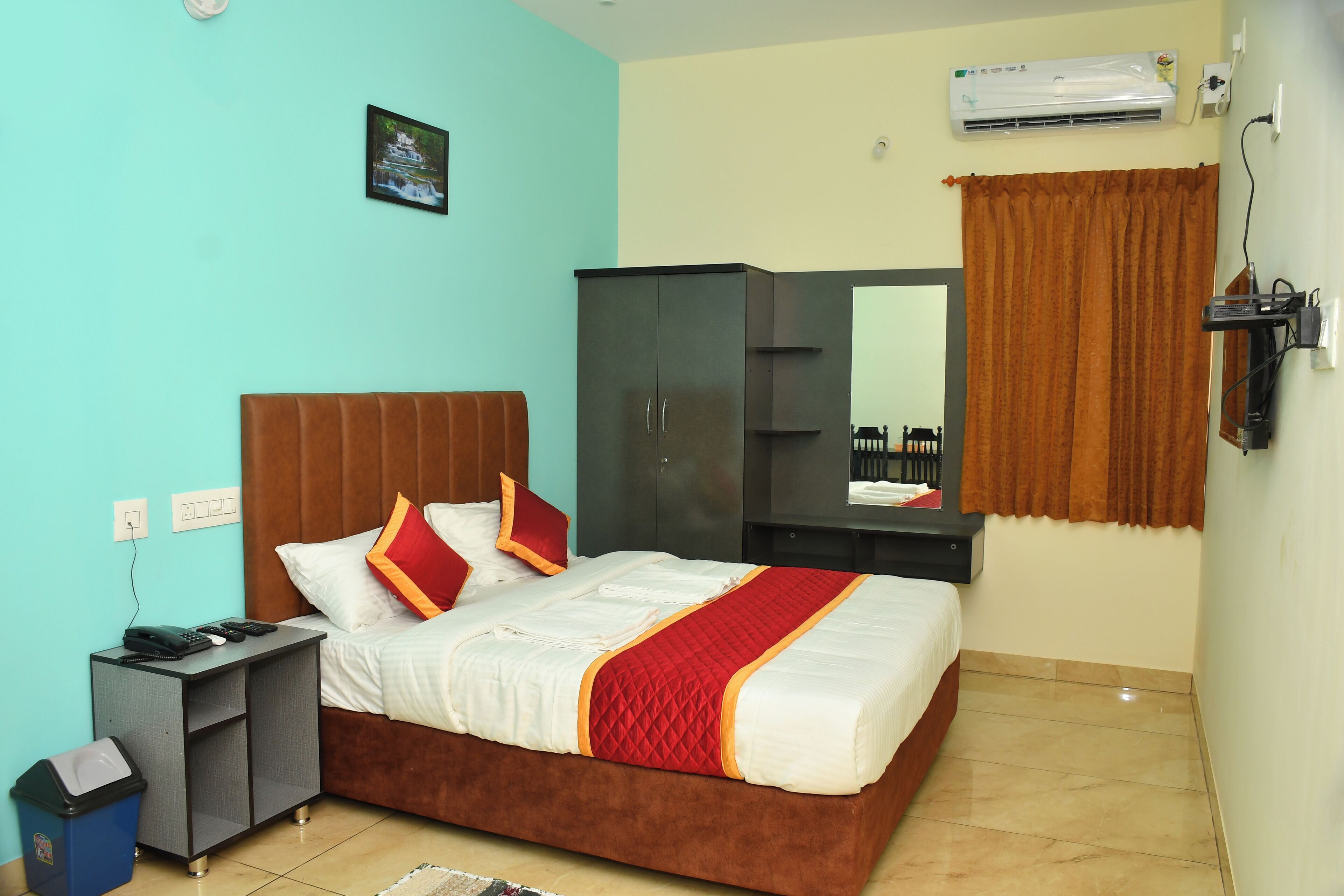 A bedroom with a bed, a wardrobe, a desk, a trash bin, and an air conditioning unit.