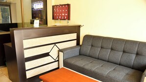 Un espace d’accueil avec un comptoir de réception sombre, un canapé gris et une table en bois.