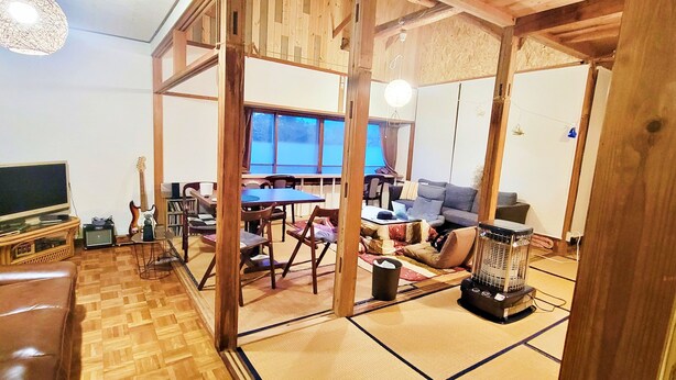 A traditional Japanese-style living room with tatami flooring, a tatami mat table, a sofa, a television, and a heater. - Guesthouse & Sharehouse carima azumik (Omachi)