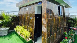 A modern building with a marble exterior, a visible entrance, and a small garden area with artificial grass and potted plants. - GUIKO Hôtel Palace  (Douala)