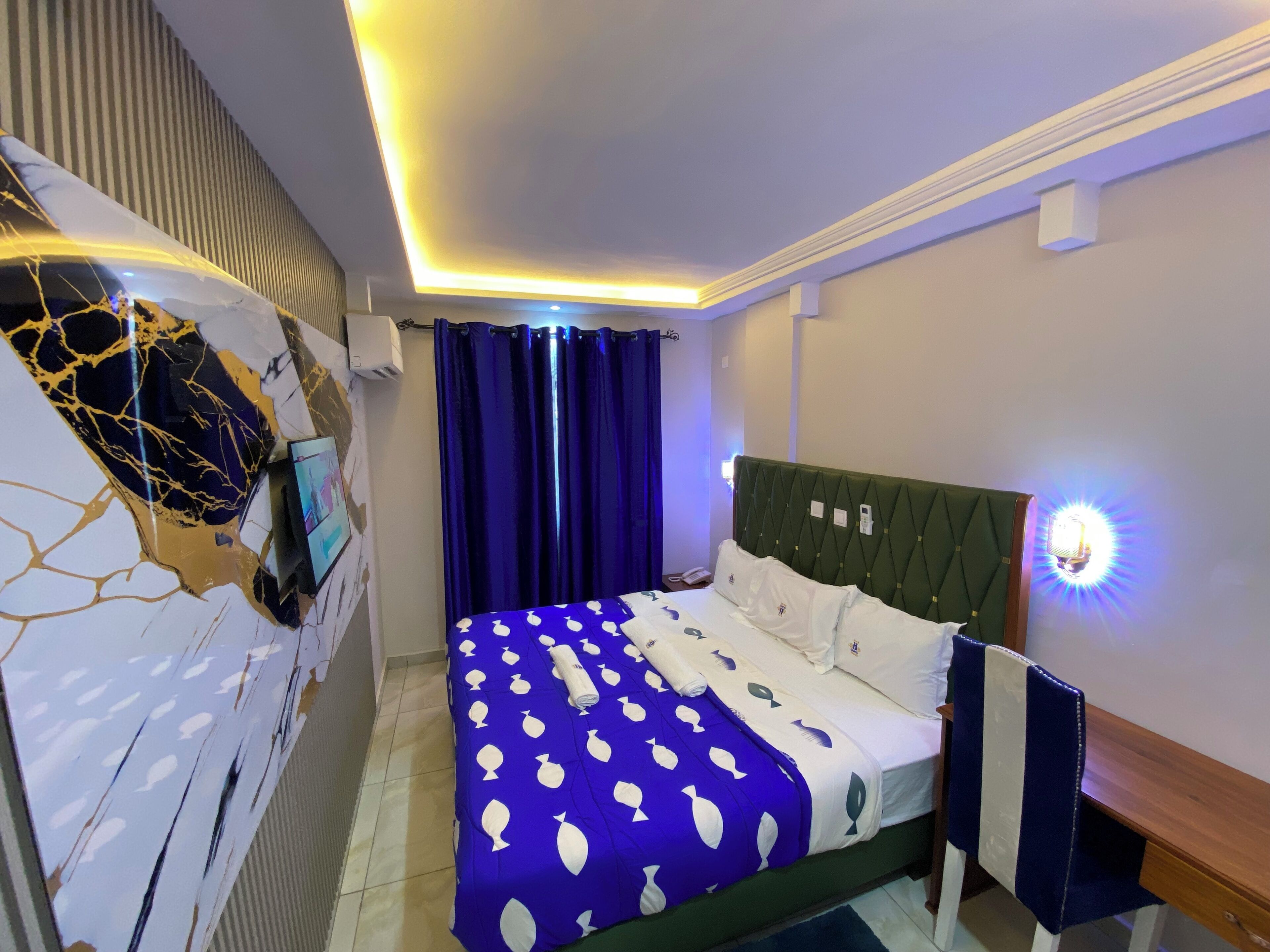 A modern hotel room with a bed, a TV mounted on the wall, and a nightstand.