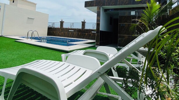 Un área de piscina con sillones blancos, un edificio moderno y una antena parabólica.