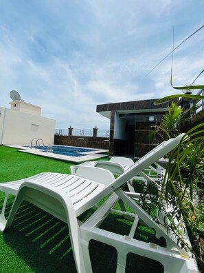 Un espace piscine avec des chaises longues blanches, un bâtiment moderne et une antenne parabolique.