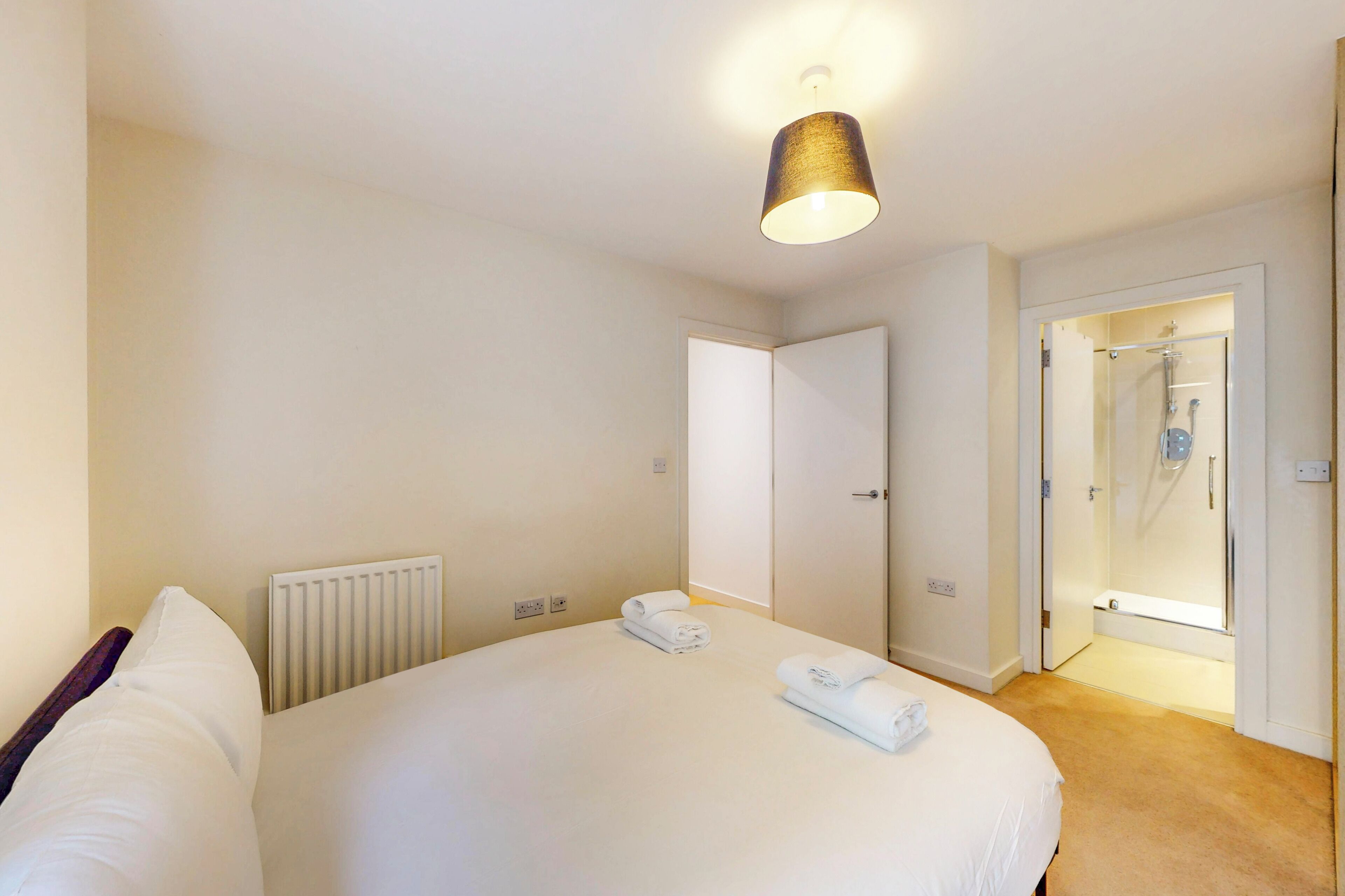 Habitación de hotel con una cama grande, un radiador, zona de ducha y una puerta que da a otra habitación.