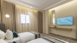 Una camera d'albergo con due letti, una televisione, uno specchio e una finestra con tende.