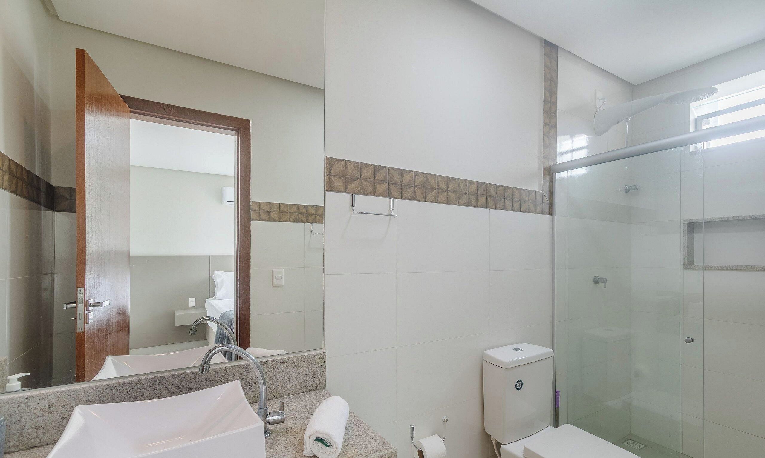 A hotel bathroom with a glass-enclosed shower, a sink with a mirror, and a toilet.