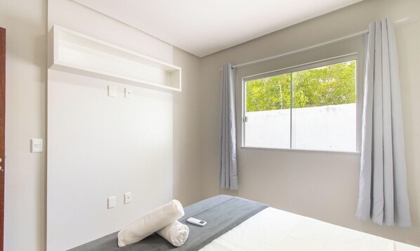 A bedroom with a bed, a window with curtains, and a wall-mounted light switch. - Apartments Near Muta Beach, BA - Rfms (Porto Seguro)