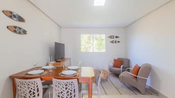 A dining area with a wooden table set for four, white chairs, and a television on a stand.