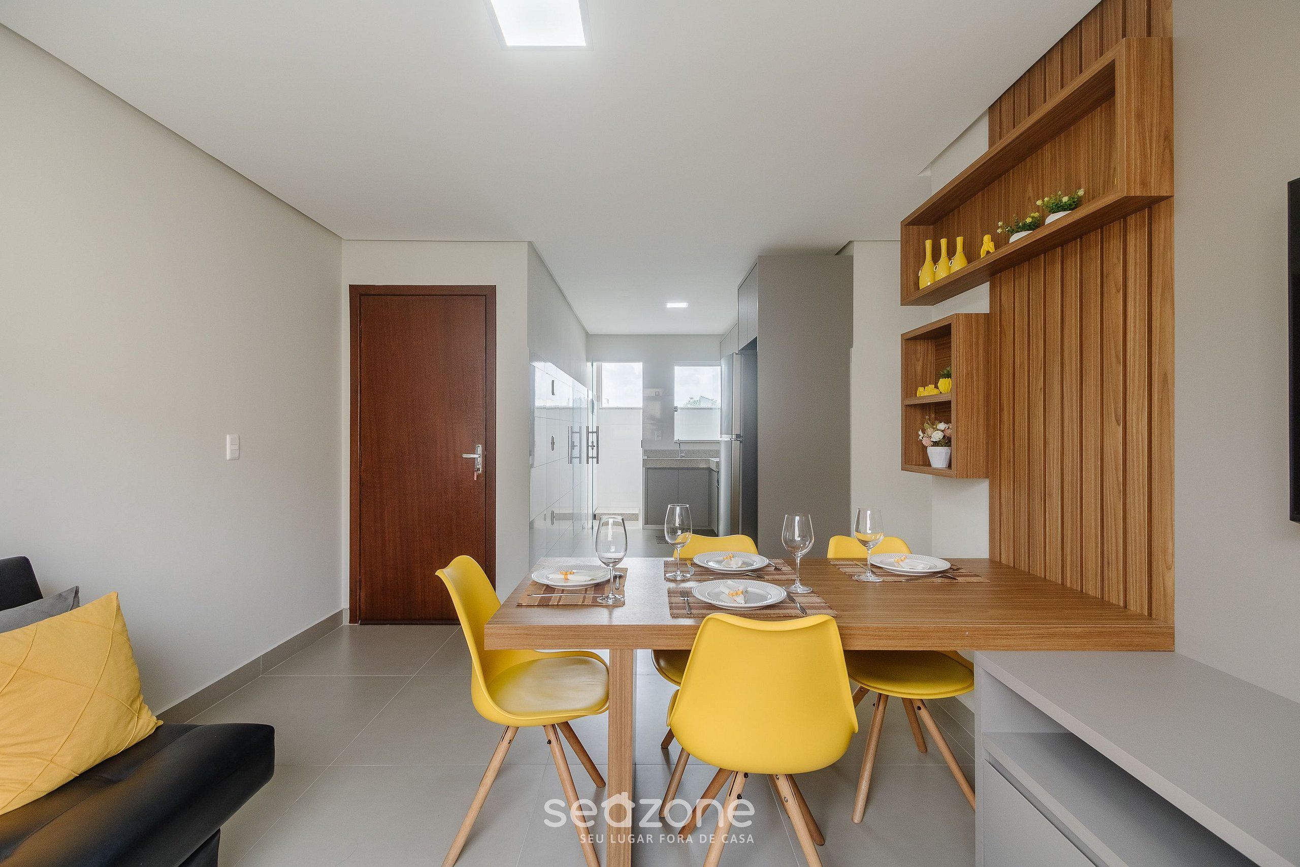 Un comedor moderno con una mesa de madera, sillas amarillas y una estantería empotrada con adornos.