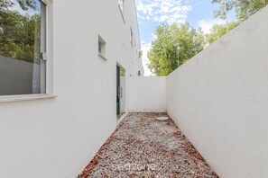 A narrow outdoor corridor with a gravel path, white walls, and a door leading to a building. - Apartments Near Muta Beach, BA - Rfms (Porto Seguro)