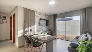 Un soggiorno moderno con zona pranzo, una TV a schermo piatto montata a parete e una porta scorrevole in vetro che dà su uno spazio esterno.