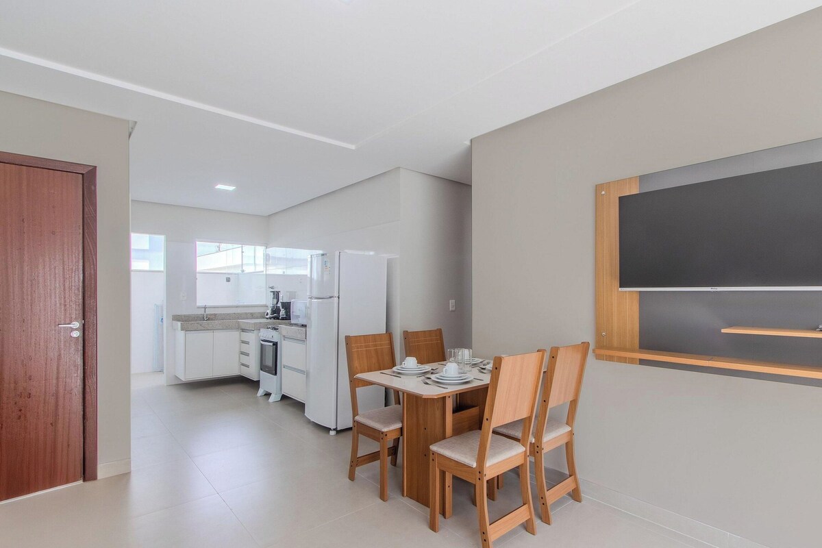 A modern kitchen with white appliances and a dining area with wooden chairs.