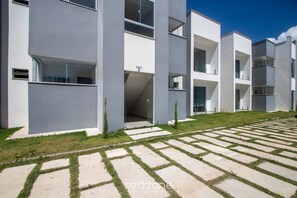 Un edificio moderno con tetto piatto, ampie finestre e un cortile pavimentato con erba e lastre di pietra.
